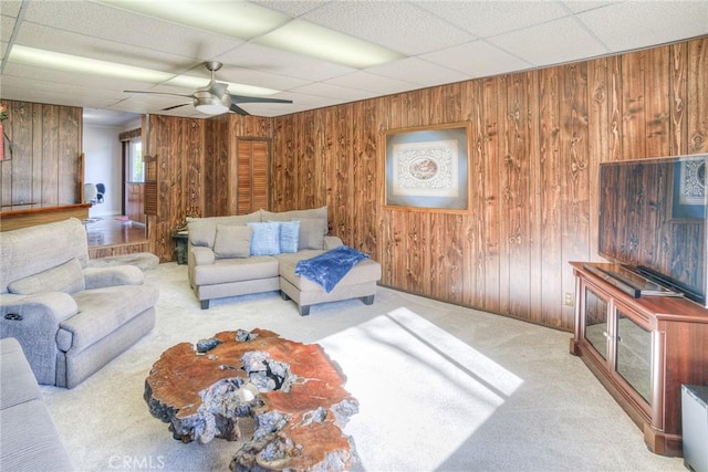 living room with wooden walls, a drop ceiling, and light colored carpet