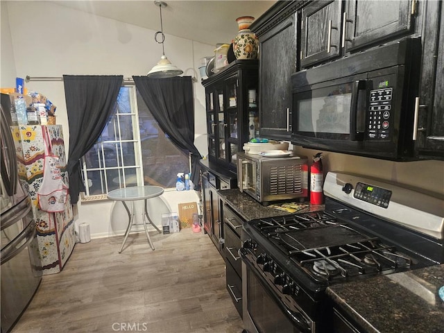 kitchen featuring black microwave, wood finished floors, dark stone countertops, freestanding refrigerator, and gas stove