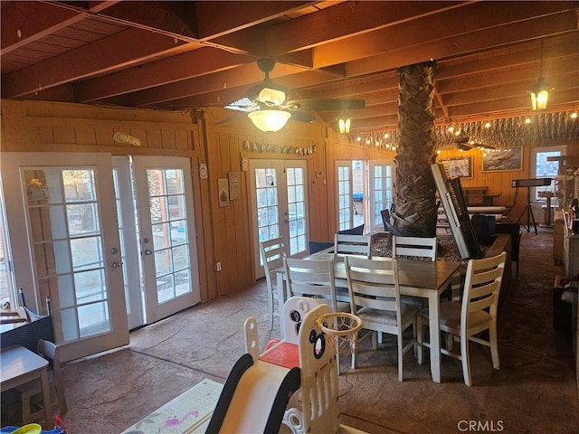 dining room with a ceiling fan, french doors, a healthy amount of sunlight, and wood walls