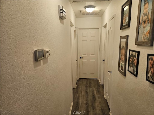 corridor with visible vents, dark wood finished floors, and a textured wall