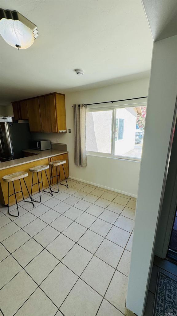 kitchen featuring a breakfast bar, light tile patterned floors, brown cabinetry, freestanding refrigerator, and baseboards