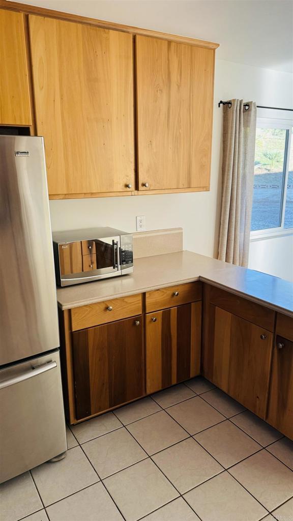 kitchen featuring light countertops, appliances with stainless steel finishes, brown cabinetry, and light tile patterned flooring