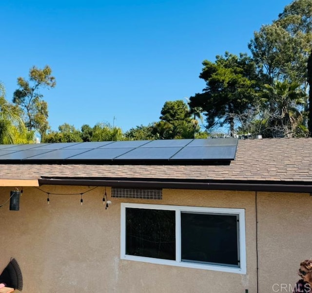 view of property exterior featuring stucco siding, roof with shingles, and solar panels