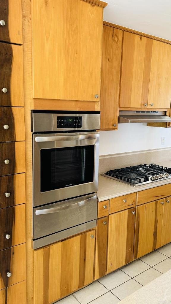 kitchen with a warming drawer, light tile patterned floors, light countertops, appliances with stainless steel finishes, and under cabinet range hood