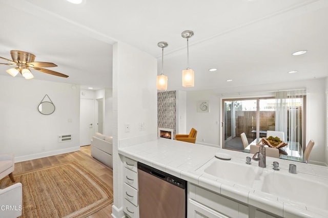 kitchen with white cabinets, a lit fireplace, light wood-type flooring, stainless steel dishwasher, and a sink