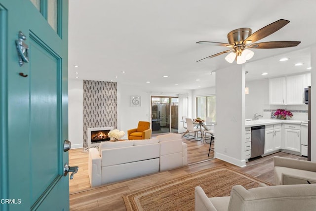 living area featuring a large fireplace, baseboards, light wood-style flooring, and recessed lighting