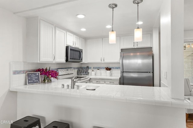 kitchen with light countertops, appliances with stainless steel finishes, a peninsula, and white cabinets