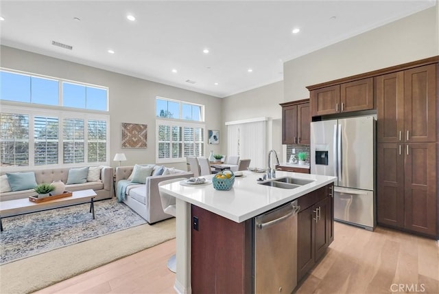 kitchen with a kitchen island with sink, a sink, open floor plan, light countertops, and appliances with stainless steel finishes