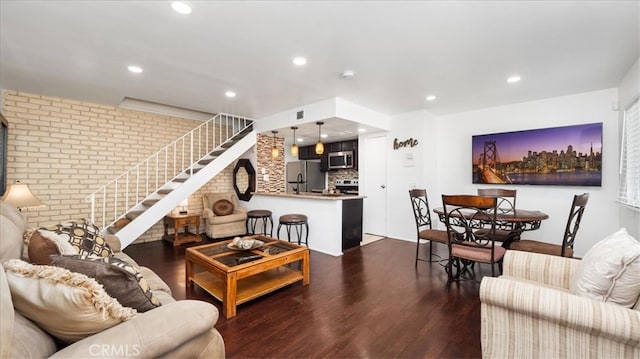 living area with dark wood-type flooring, recessed lighting, stairway, and brick wall