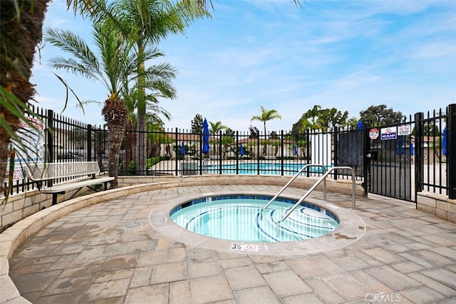 view of swimming pool with fence and a hot tub