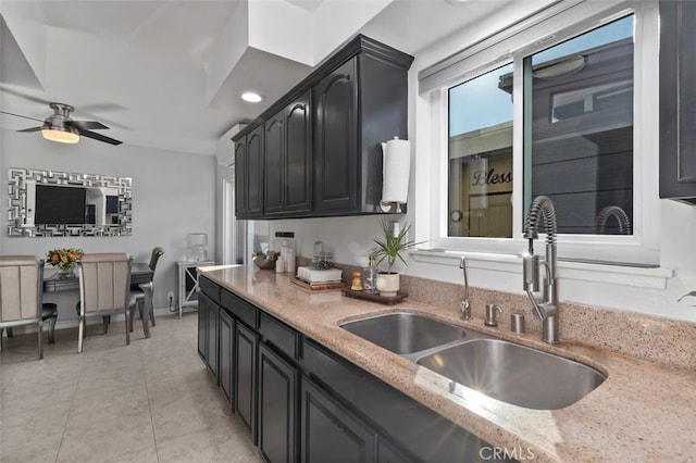 kitchen with light tile patterned floors, a sink, ceiling fan, dark cabinetry, and baseboards