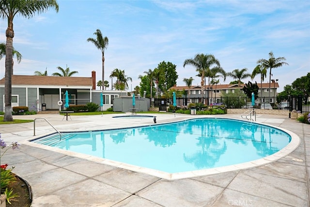 community pool featuring fence, a hot tub, and a patio