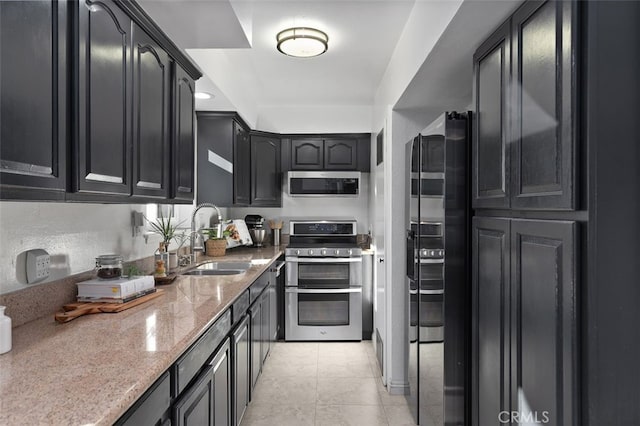 kitchen featuring stainless steel appliances, a sink, light stone countertops, and dark cabinets