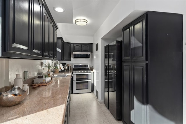 kitchen with light tile patterned floors, stainless steel appliances, a sink, light stone countertops, and dark cabinetry