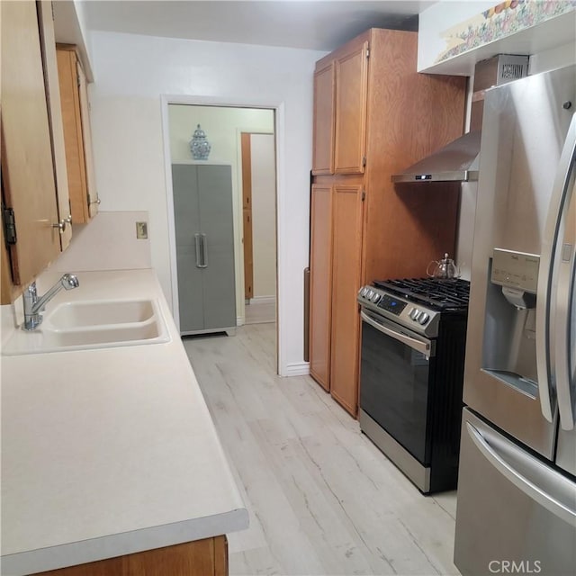 kitchen featuring light wood finished floors, light countertops, brown cabinets, stainless steel appliances, and a sink