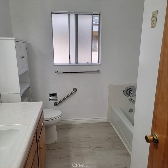 full bathroom featuring toilet, wood finished floors, baseboards, a bath, and vanity