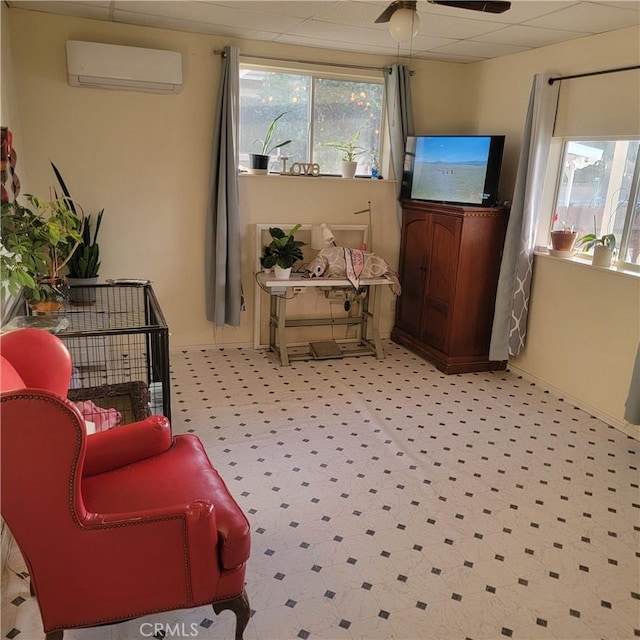 living area with plenty of natural light, a ceiling fan, a wall unit AC, and a drop ceiling