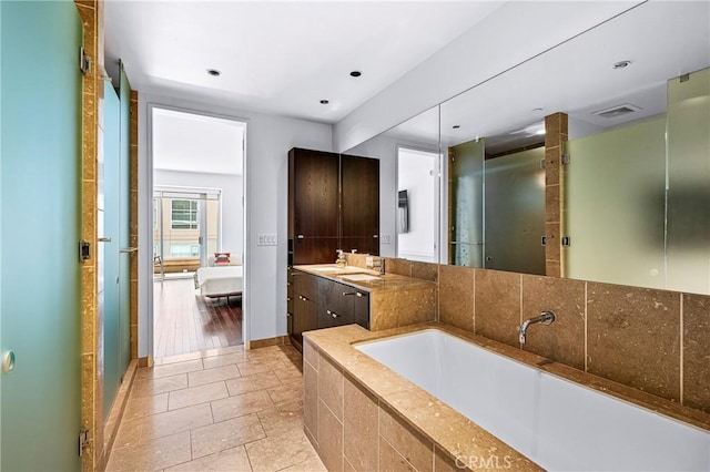 ensuite bathroom featuring baseboards, connected bathroom, a garden tub, vanity, and a shower stall