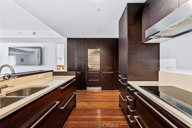 kitchen featuring wall chimney range hood, modern cabinets, light countertops, and a sink