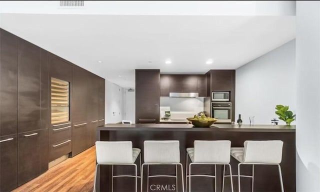 kitchen with light wood-style flooring, stainless steel appliances, visible vents, dark brown cabinets, and modern cabinets