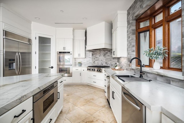 kitchen featuring built in appliances, a sink, white cabinets, custom exhaust hood, and tasteful backsplash