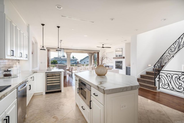 kitchen with wine cooler, white cabinetry, hanging light fixtures, appliances with stainless steel finishes, and a center island