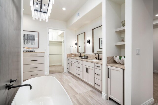 bathroom with a sink, visible vents, a freestanding bath, a spacious closet, and double vanity