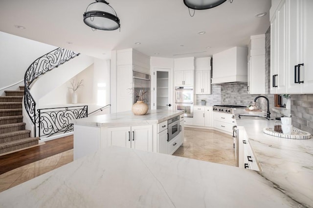 kitchen with appliances with stainless steel finishes, white cabinets, a kitchen island, a sink, and premium range hood