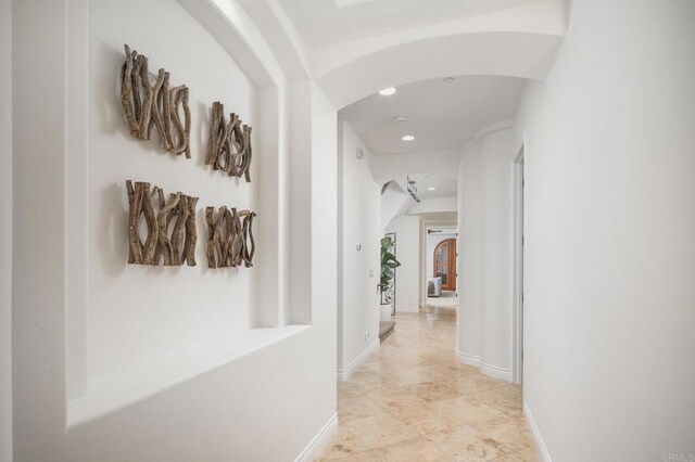 corridor with arched walkways, recessed lighting, and baseboards