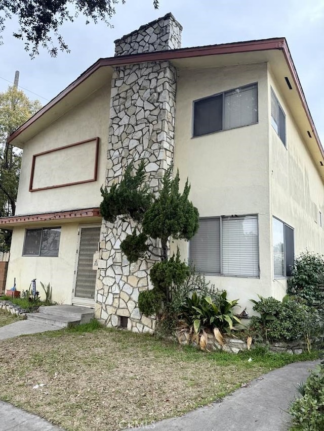 view of front of property with stone siding, a chimney, and stucco siding