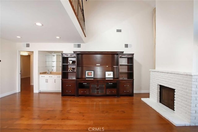 unfurnished living room with a brick fireplace, baseboards, visible vents, and dark wood-style flooring