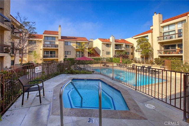 community pool with a patio area, fence, and a hot tub