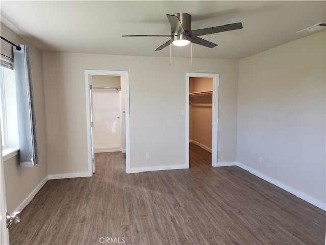 unfurnished bedroom with baseboards, a spacious closet, multiple windows, and wood finished floors