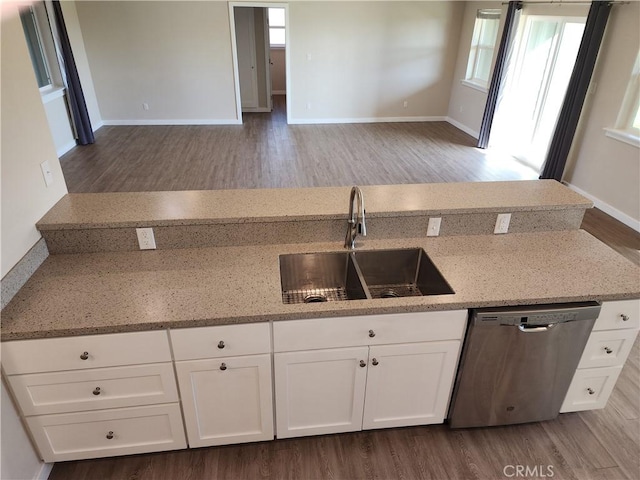 kitchen with stainless steel dishwasher, wood finished floors, a sink, light stone counters, and white cabinets