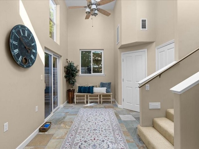 interior space with stairway, baseboards, visible vents, a high ceiling, and ceiling fan