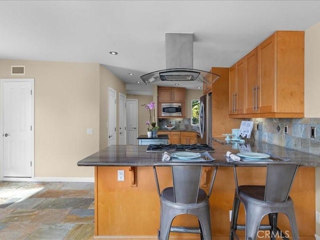 kitchen with brown cabinets, appliances with stainless steel finishes, a peninsula, and island range hood