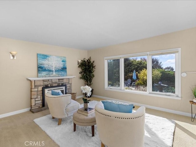 sitting room with a stone fireplace, a healthy amount of sunlight, baseboards, and light carpet