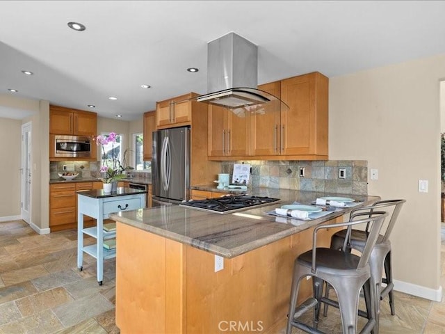 kitchen with brown cabinetry, a peninsula, island exhaust hood, stainless steel appliances, and tasteful backsplash