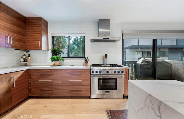 kitchen with light wood finished floors, light countertops, brown cabinetry, wall chimney range hood, and high end stove