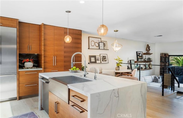 kitchen with a center island with sink, brown cabinetry, modern cabinets, decorative light fixtures, and built in fridge