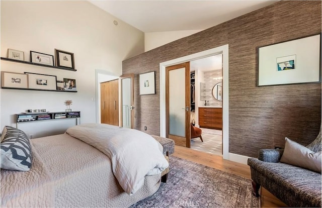 bedroom featuring connected bathroom, high vaulted ceiling, and wood finished floors