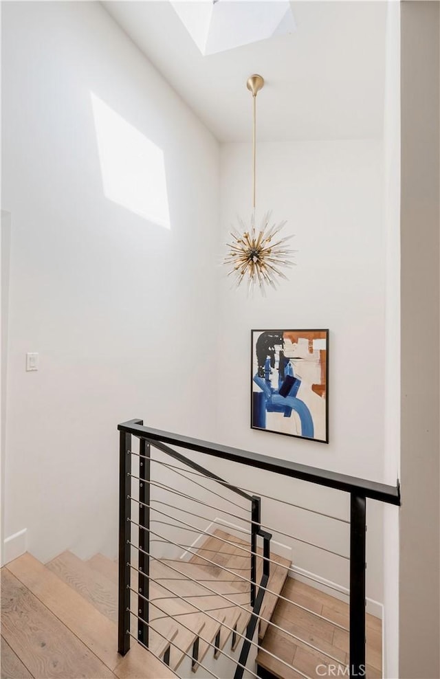 stairway featuring a skylight, an inviting chandelier, baseboards, and wood finished floors