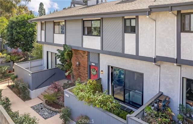 exterior space featuring stucco siding, a shingled roof, and brick siding