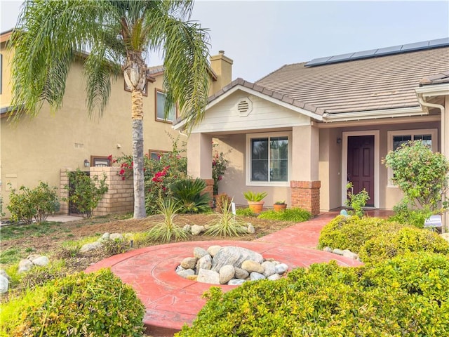 entrance to property featuring solar panels, a chimney, a tile roof, and stucco siding