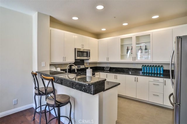 kitchen featuring stainless steel appliances, white cabinetry, a peninsula, and a kitchen bar