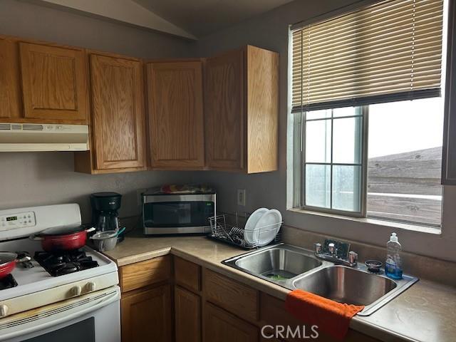 kitchen featuring white range with gas stovetop, under cabinet range hood, a sink, light countertops, and stainless steel microwave