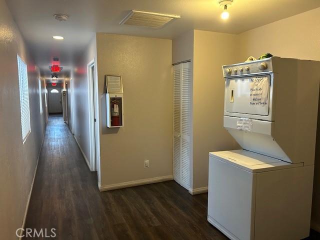 washroom with laundry area, dark wood-style flooring, stacked washing maching and dryer, and baseboards