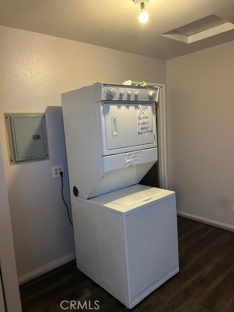 laundry room featuring laundry area, baseboards, stacked washing maching and dryer, electric panel, and dark wood finished floors