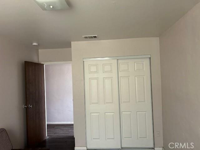 unfurnished bedroom featuring dark wood-type flooring, a closet, and visible vents