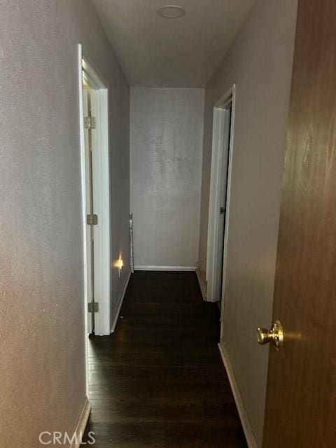 corridor featuring baseboards and dark wood-style flooring